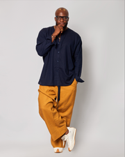 A man wearing a navy linen shirt and mustard full-length wide trousers with a pair of white sneakers.